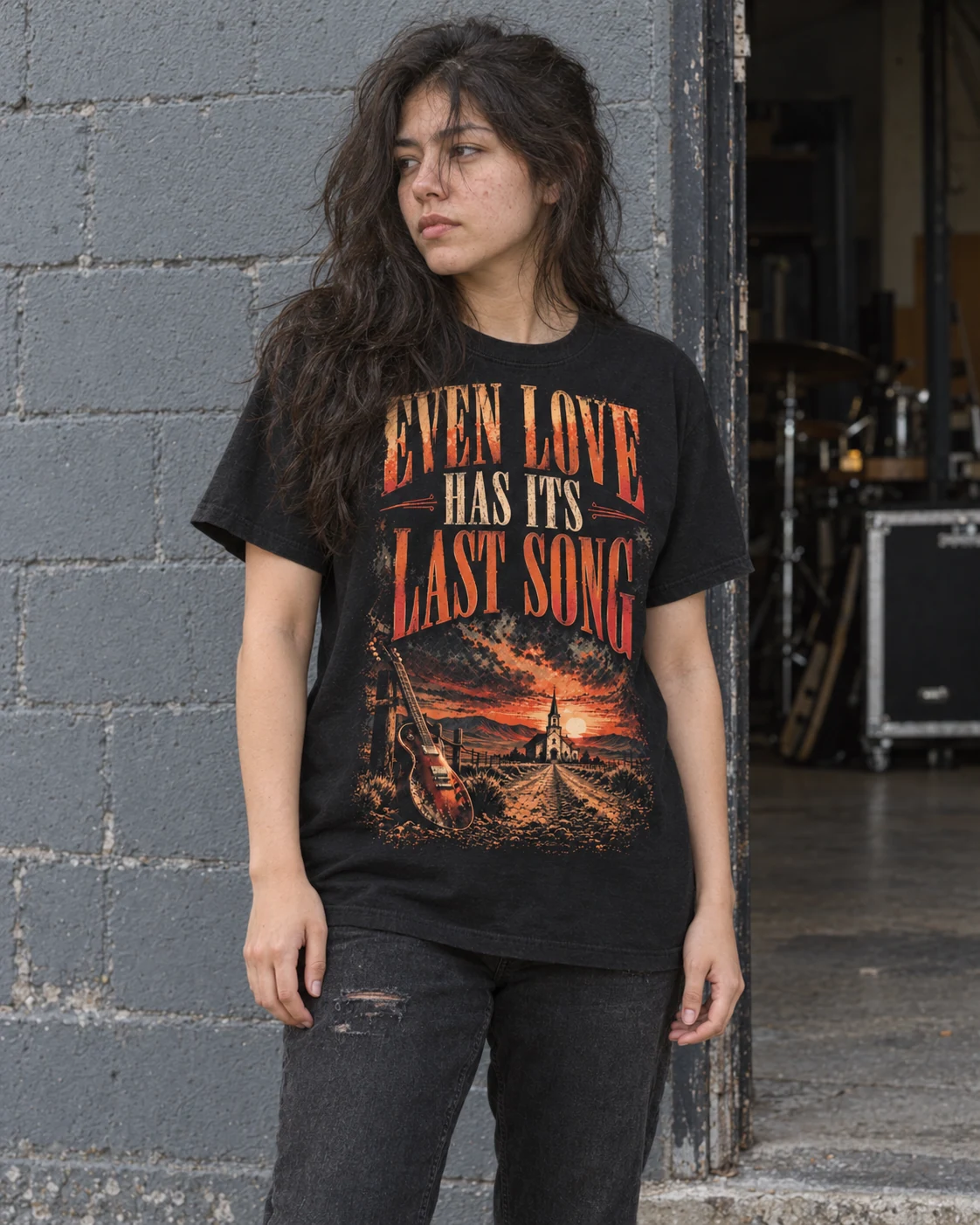 Una mujer lleva la camiseta Última Canción junto a una entrada de bloques grises, con luz natural